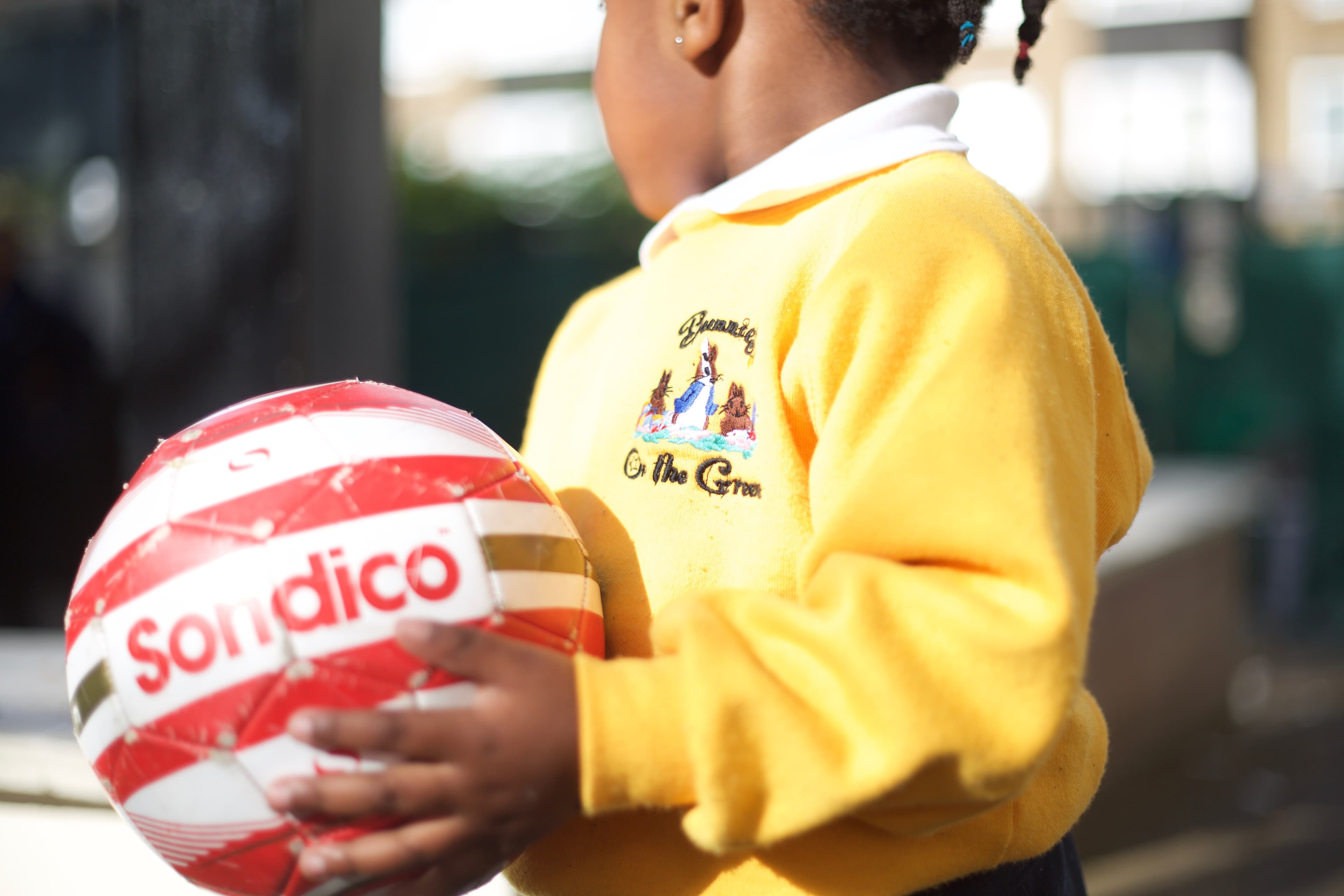 Child in Bunnies on the Green uniform holding a football outdoors